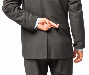 A person in a dark gray suit is seen from behind with their right hand crossing fingers behind their back, reminiscent of those tense moments in performance reviews where truth may be hidden or promises are made without intention to keep them.