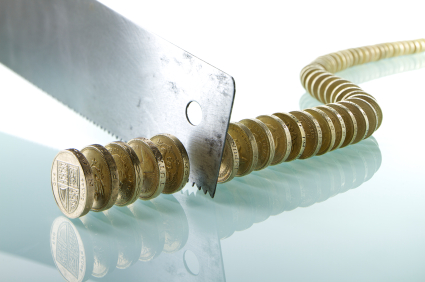 A saw cutting into a stack of British one pound coins arranged in a spiral on a reflective surface, symbolizing the organization's financial cuts or economic challenges.