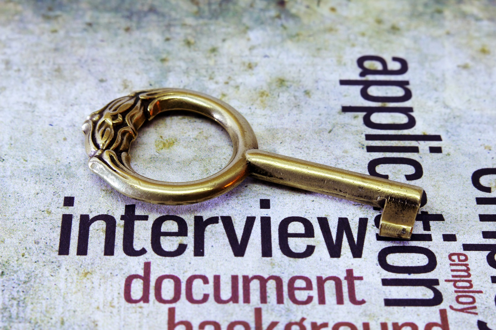 A vintage brass key with an ornate handle is resting on a textured surface with the words "interview", "application", "document", and "background" in different fonts and orientations, evoking a sense of governmental history.
