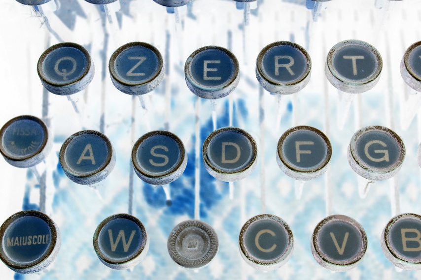 An inverted (negative) image of a vintage typewriter keyboard featuring a QWERTY layout. The keys appear in shades of blue and white, with some letters and symbols clearly visible, such as Q, W, E, R, T, Y, A, S, D, F, G. The word "MAIUSCOLE" stands out prominently on the left like a government