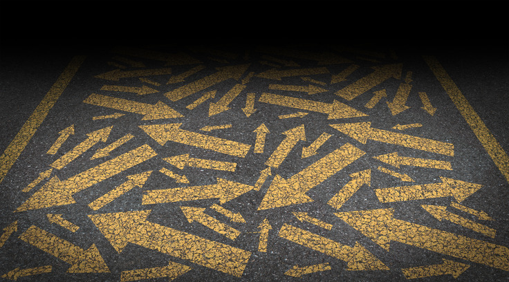 A road surface is covered with numerous overlapping yellow arrows pointing in different directions, creating a chaotic and confusing pattern reminiscent of a challenging career move. The top of the image fades to black, emphasizing the disorder of the arrows.