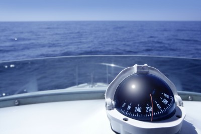 A nautical compass on a boat's dashboard points southwest with an expansive view of the ocean and a clear blue sky in the background. The scene conveys a sense of navigation and open water exploration, symbolizing the embarking on an adventurous career path.