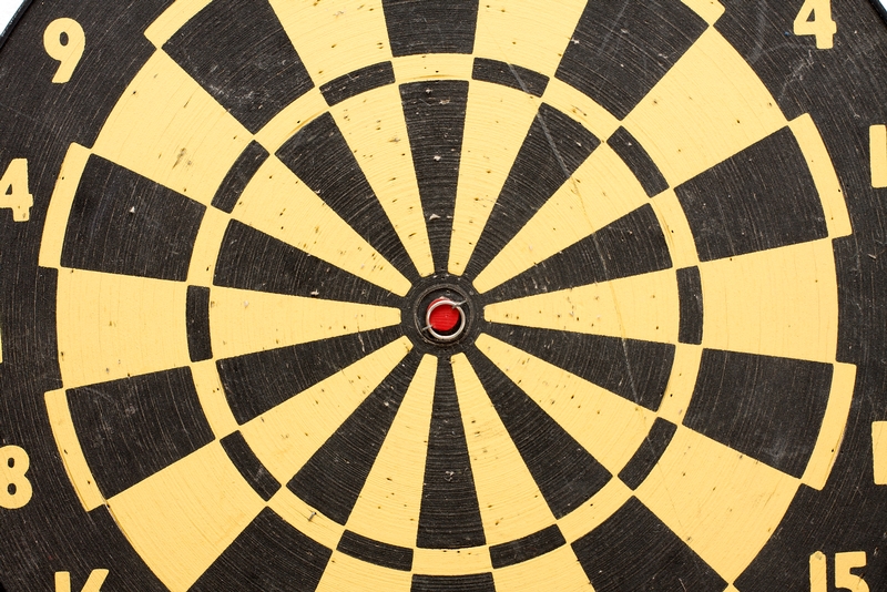 Close-up of a dartboard showcasing the bullseye in the center, symbolizing precision and performance goals. The dartboard features alternating black and yellow triangular sections, with numbers 1 through 9 visible on the outer edge. The bullseye area is red, surrounded by a black circle.