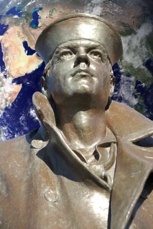 A bronze statue of a sailor, donning a cap and a coat with a large collar, looking upward. In the background, an image of Earth with visible continents and oceans underscores a global military theme.