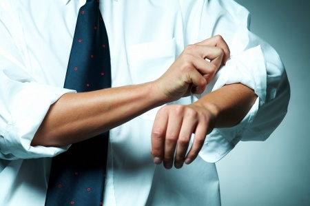 A person wearing a white dress shirt and dark tie is rolling up their sleeves, likely preparing for an interview. Their hands and forearms are visible as they focus on adjusting the cuff of the sleeve, set against a neutral, light-shaded background.