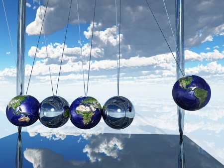 A Newton's cradle with spheres designed to look like Earth, demonstrating momentum against a backdrop of a blue sky with clouds. The cradle's base reflects the spheres and the sky, creating a mesmerizing mirrored effect.