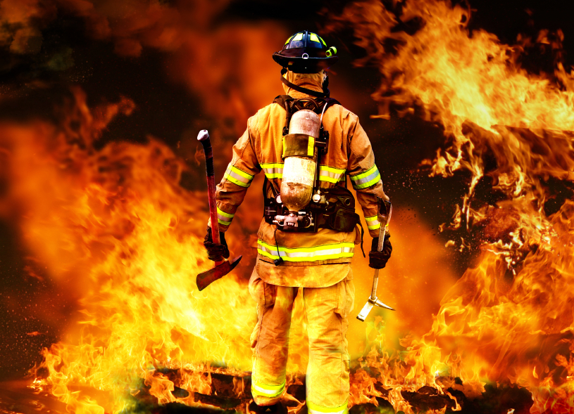 A firefighter wearing full protective gear, including an oxygen tank and helmet, faces away while surrounded by intense flames. He holds an axe in his right hand and a crowbar in his left hand, appearing poised to tackle the blaze—a striking image for any Fire Service Resume.