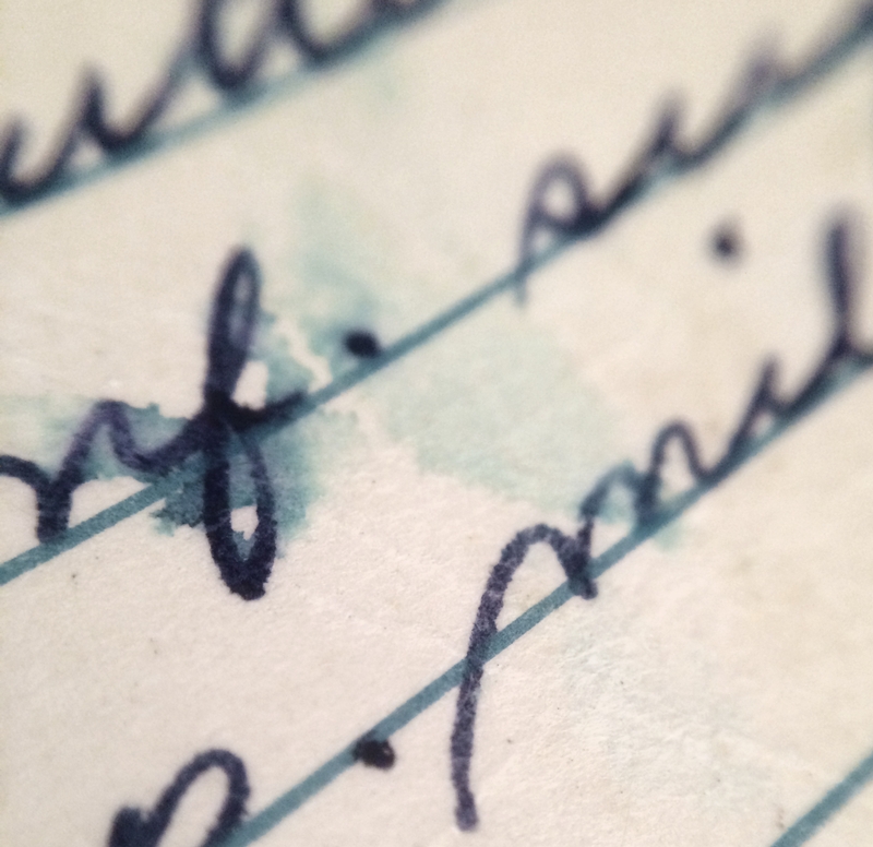 A close-up of cursive writing on lined paper, with black ink slightly smudged and tinted by a light blue water stain. The letter's ink appears to have bled into the paper around the wet area, creating an abstract pattern.