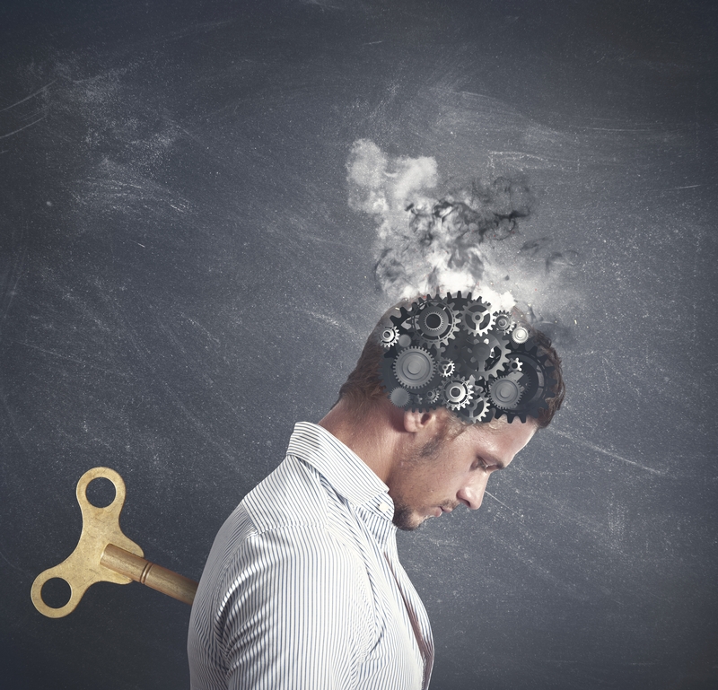 A man in a striped shirt is depicted with gears and smoke emerging from his head, symbolizing intense thought or mental pressure. A large wind-up key is inserted into his back, suggesting a mechanical or robotic element to his existence, emblematic of the grind of meaningless work.