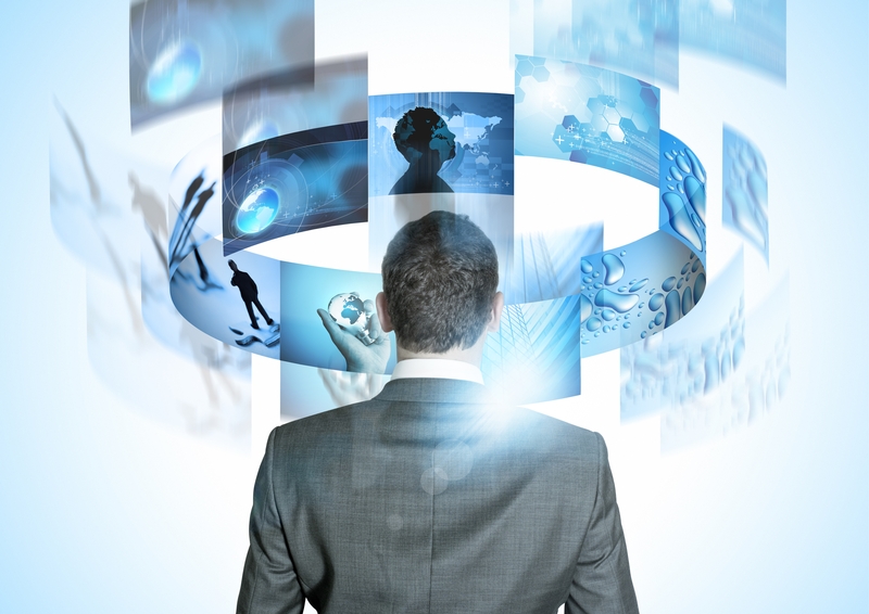 A man in a suit stands facing away, looking at floating digital screens arranged in a semi-circle. The screens display various futuristic images, including silhouettes, a world map, scientific symbols, and abstract designs, all reflecting new technologies. The overall color scheme is blue and white.
