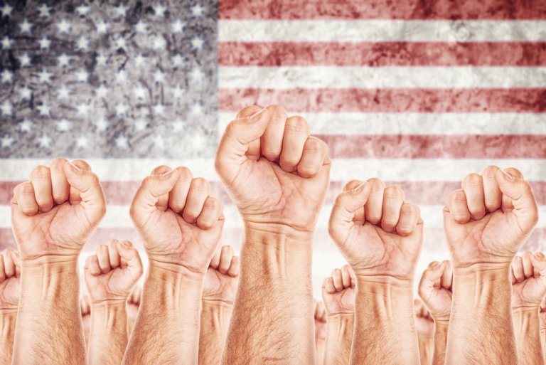 A group of raised fists in solidarity, representing American workers, is depicted against a backdrop of a blurred American flag. The image conveys a sense of unity, strength, and collective action.