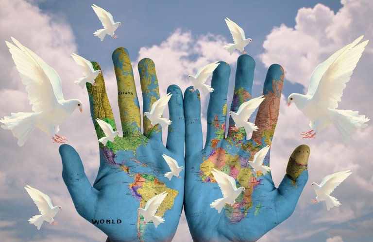 Two hands painted with a map of the world are held up against a cloudy sky. White doves are flying around the hands, symbolizing peace and unity, as if illustrating global projects envisioned in harmony.