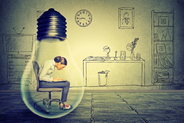 A woman sits in a chair while working on a laptop inside a giant light bulb. The background features a hand-drawn style office with a clock, bookshelves, desks, and computer. The overall image depicts the creative workspace concept essential for effective crisis leadership.
