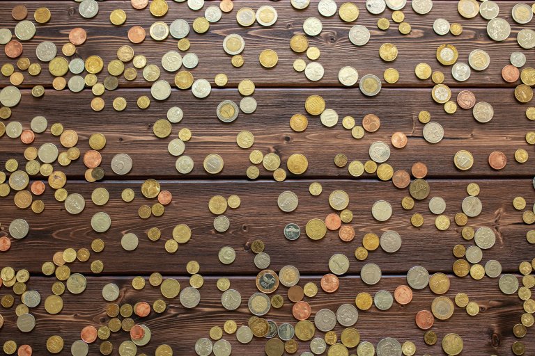 A scattered collection of various coins of different sizes and colors spread across a wooden surface.