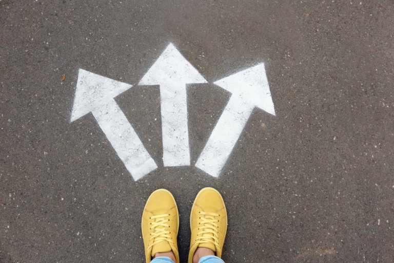 Yellow shoes standing at a junction with three painted white arrows on the asphalt, pointing left, right, and straight ahead, symbolizing choices in careers in government.