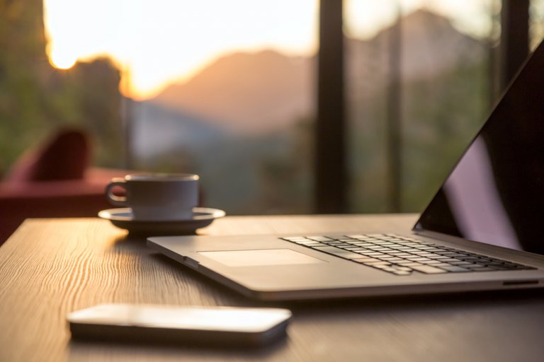 A close up of a cell phone, a laptop and a cup