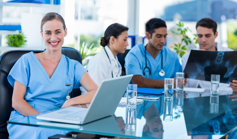 Happy doctor smiling at the camera while her colleagues analyzes an xray
